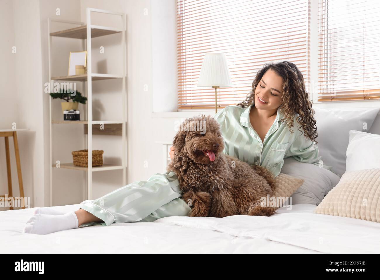 Young woman with cute poodle lying in bedroom Stock Photo