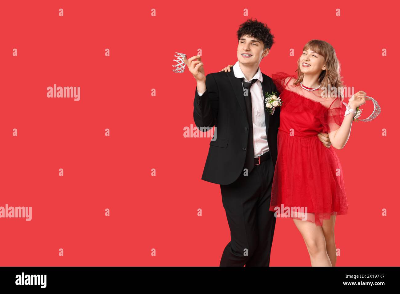 Happy prom couple holding crowns on red background Stock Photo