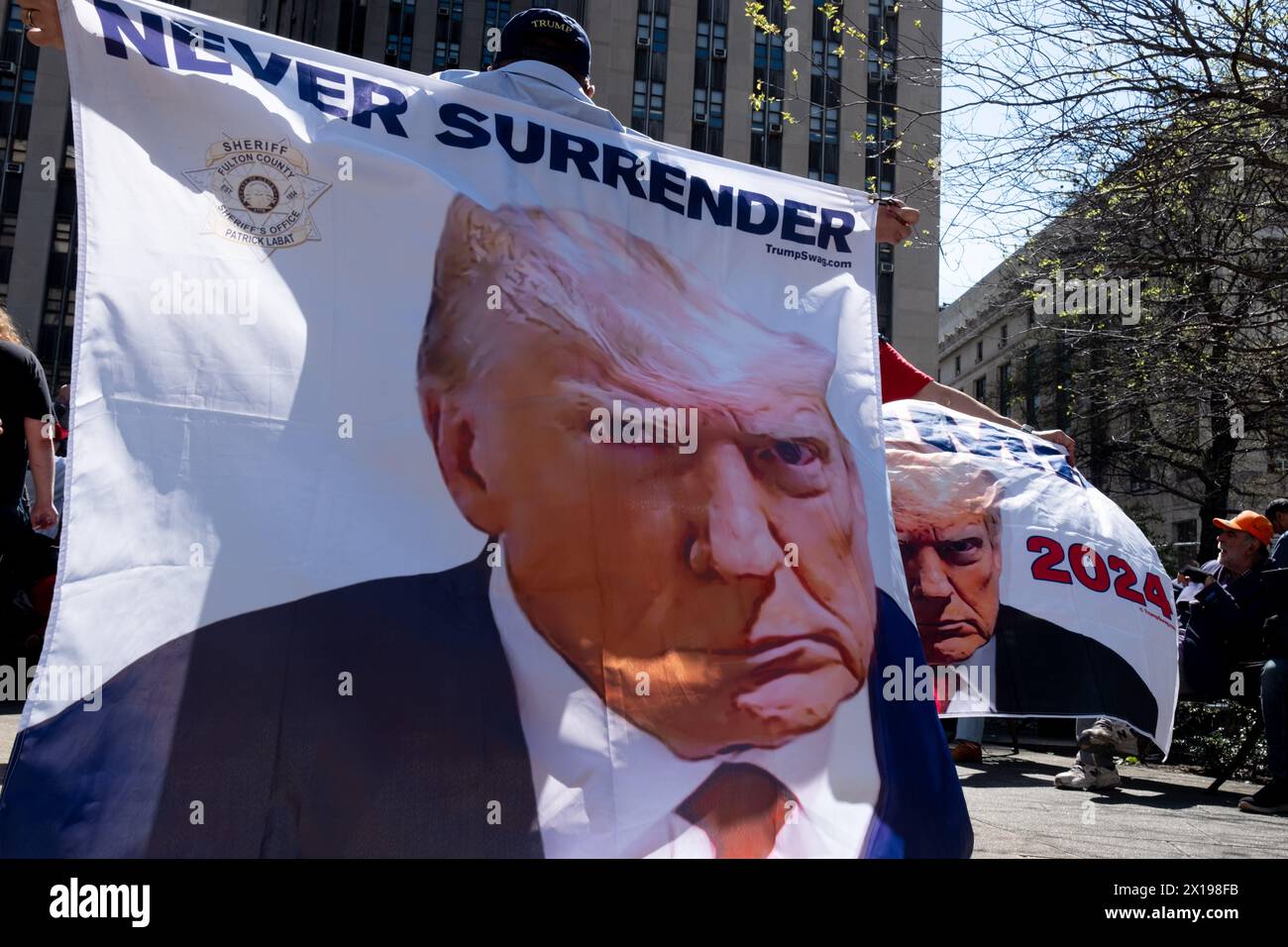 New York, United States. 15th Apr, 2024. Two men holding large Trump banners, one says 'Never Surrender' the other says 'Trump 2024' Trump supporters gathered across from the courthouse where jury selection begins for the trial of former President Donald Trump. Trump faces felony charges related to hush money paid to adult film actress Stormy Daniels. This is the first time in US history any former president will be tried on criminal charges. Credit: SOPA Images Limited/Alamy Live News Stock Photo