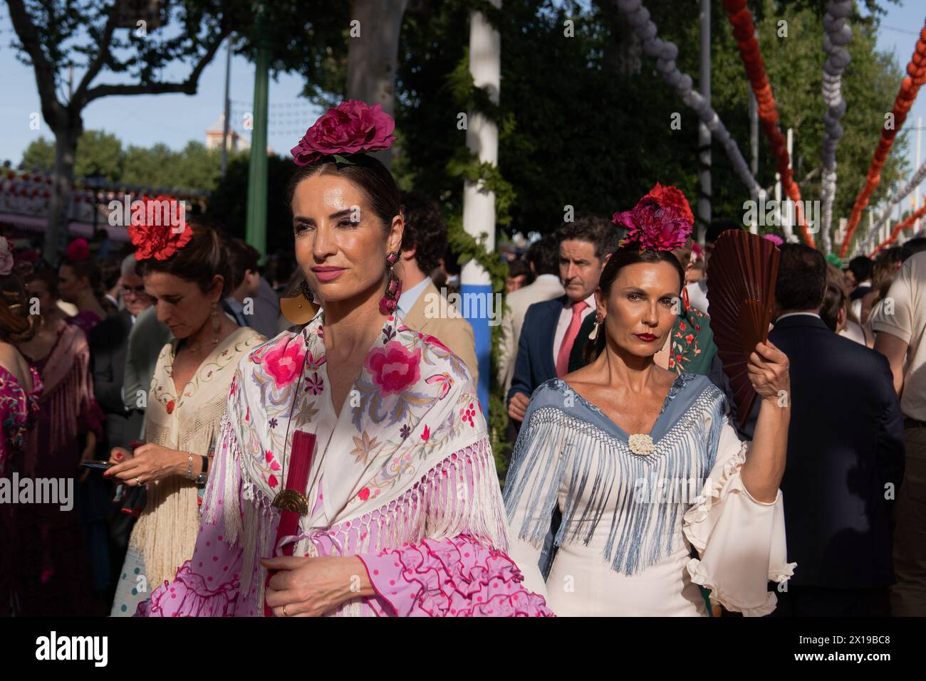 Women wearing the traditional flamenco dresses, often in bright colors, and accessorized with flowers in their hair are seen laughing during the fair. The April Fair is one of the most international and popular festivals in Seville. Created in 1847 as a livestock fair, over time the festive aspect of the event ended up taking over the commercial part, until it became an essential event for Sevillians. For a week, more than a thousand booths installed in the fairgrounds became the second home of the inhabitants of this city, a space where they can share and have fun in company until the early h Stock Photo