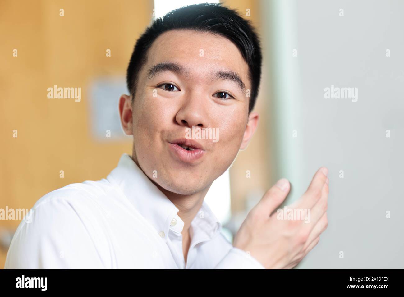 A student in a white dress shirt is gesturing and talking to the camera in the classroom. The camera is the point of view of his neighbor chatting wit Stock Photo