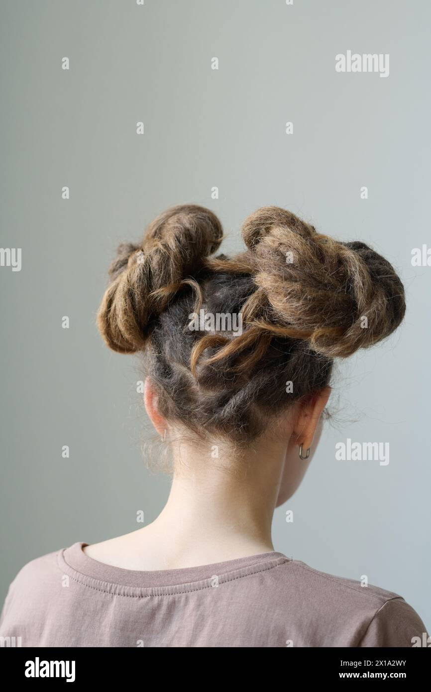Vertical back view of young woman with dreadlocks space buns hairstyle ...