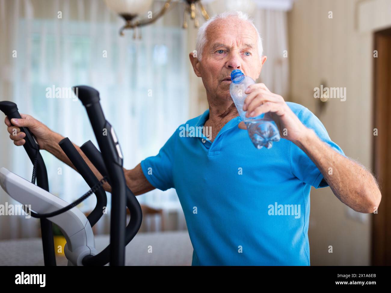 Senior man using elliptical trainer and drinking water Stock Photo