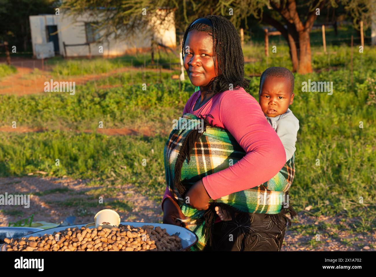 young village street vendor african woman with braids holding her baby in the back Stock Photo