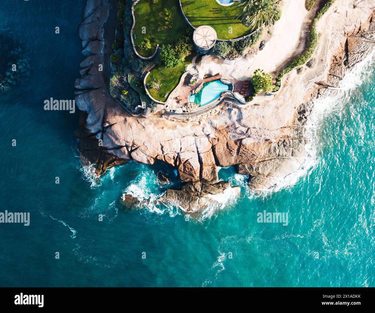 Drone view of a cliff edge with green grass surrounded by blue ocean water. Stock Photo