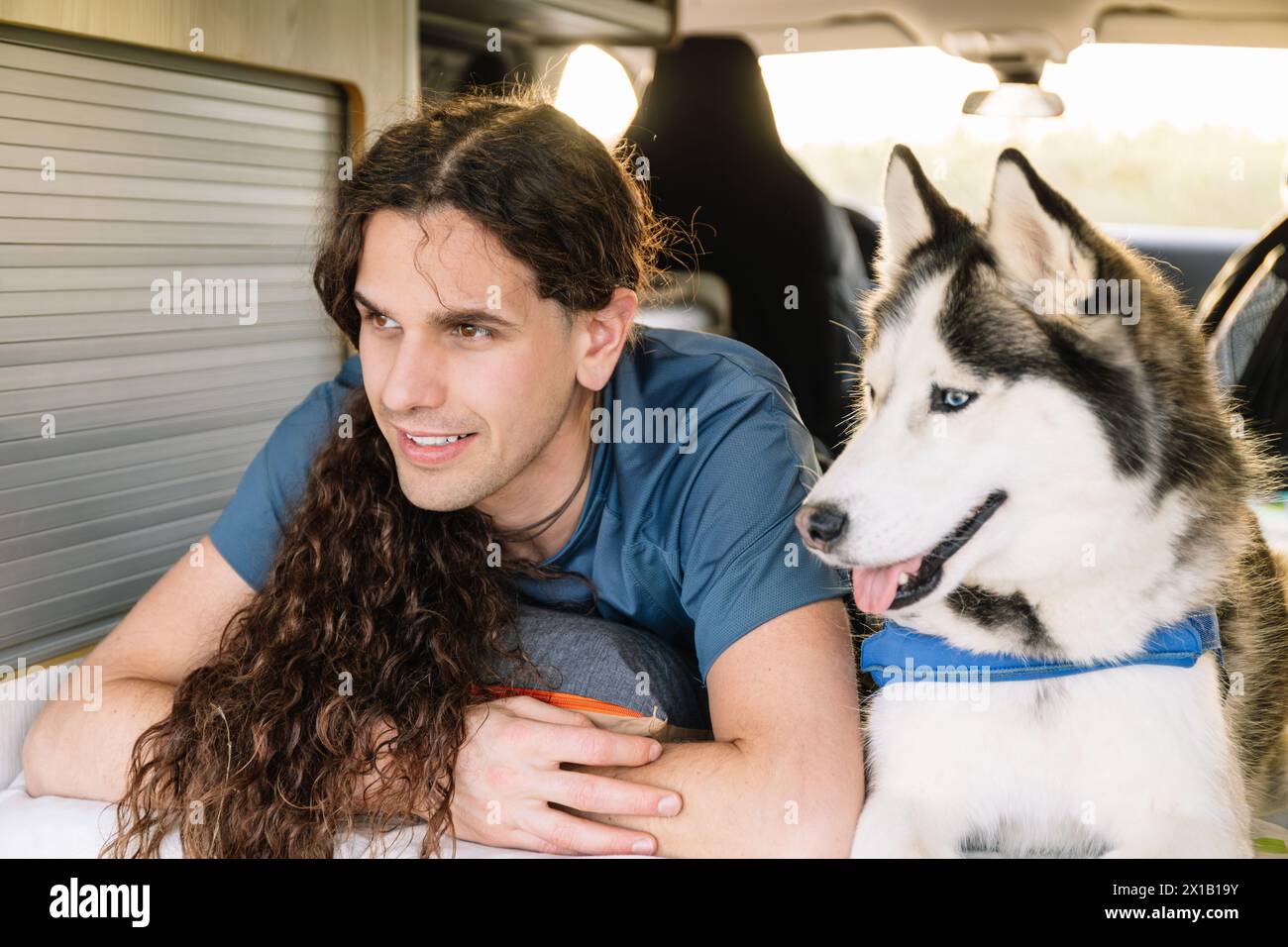 Horizontal photo a man with luscious curly hair shares a relaxed moment with his joyful husky inside the comfortable space of their modern c Stock Photo