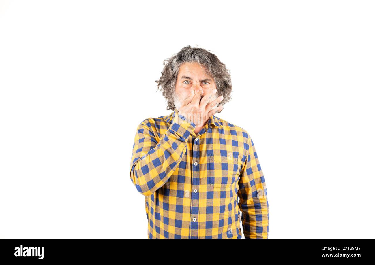 Bearded man in checkered shirt smelling something smelly and disgusting holding his breath with fingers in his nose, bad smell Stock Photo