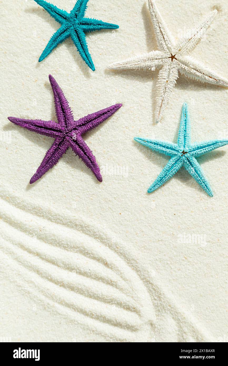 Colored starfish on white fine sand. Summer background, free space for your decoration, flat lay. Stock Photo