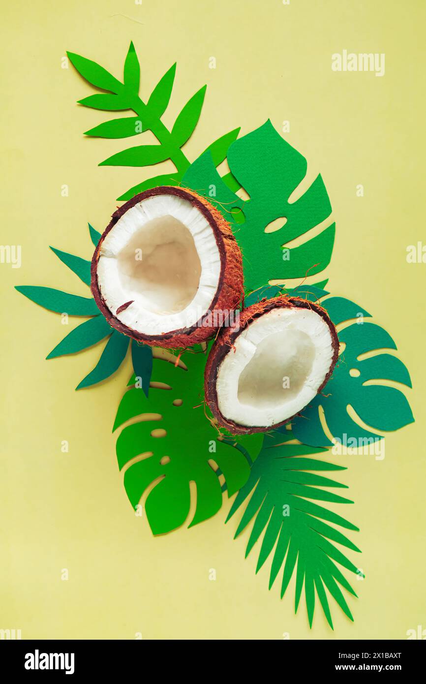 Broken coconut and paper tropical leaves on a light yellow background. Summer background, flat lay. Stock Photo