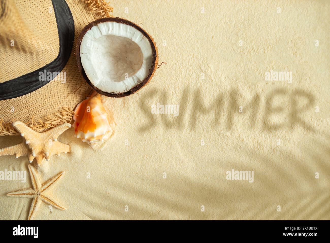Straw hat, coconut, starfish, shells, shadow of a palm tree and the inscription SUMMER on the sand. Summer background, free space for decoration, flat Stock Photo