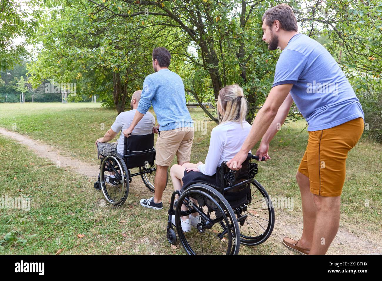 A heartwarming scene of four friends, including two using wheelchairs, spending quality time together outdoors in a lush green park. Stock Photo