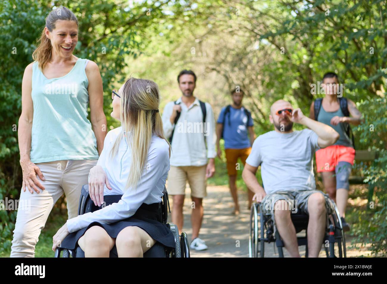 A diverse group of friends in a park setting, featuring two persons using wheelchairs and a woman with a knee prosthetic, showcasing inclusion and acc Stock Photo