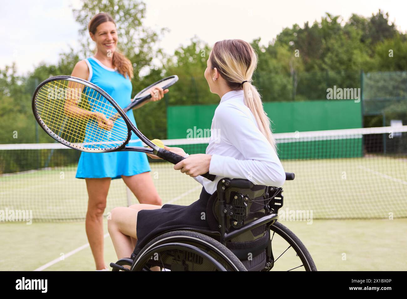 Two people enjoying a game of tennis, one person who uses a wheelchair showing active lifestyle and inclusion on an outdoor court. Stock Photo