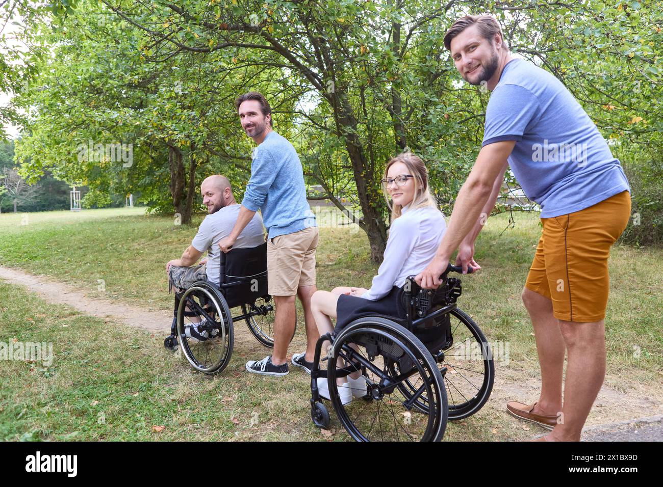 Group of friends, including people using wheelchairs, sharing a joyful time together outdoors surrounded by greenery. Stock Photo