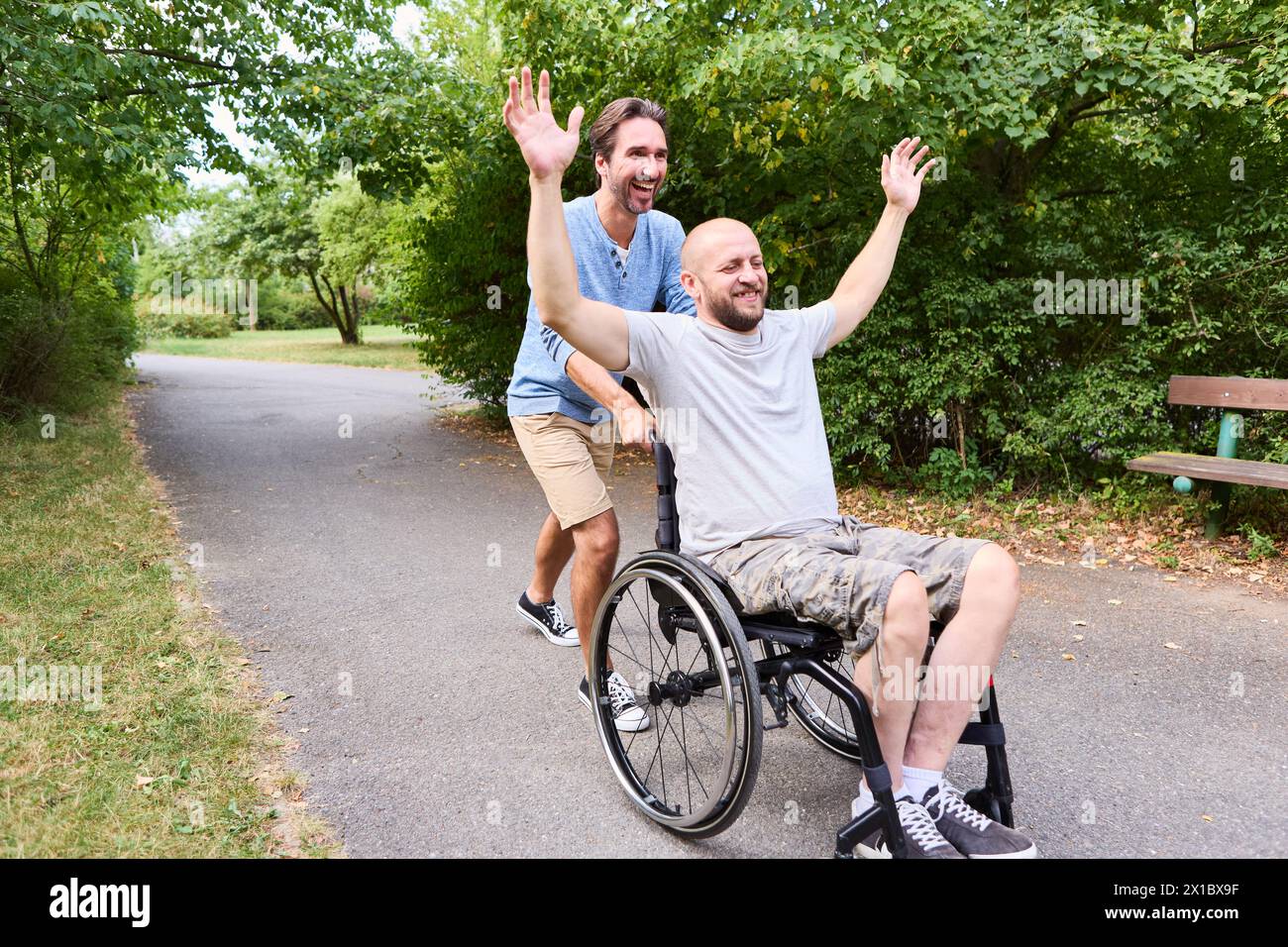 A person who uses a wheelchair and his companion are having a joyful time together outdoors, expressing happiness and friendship. Stock Photo