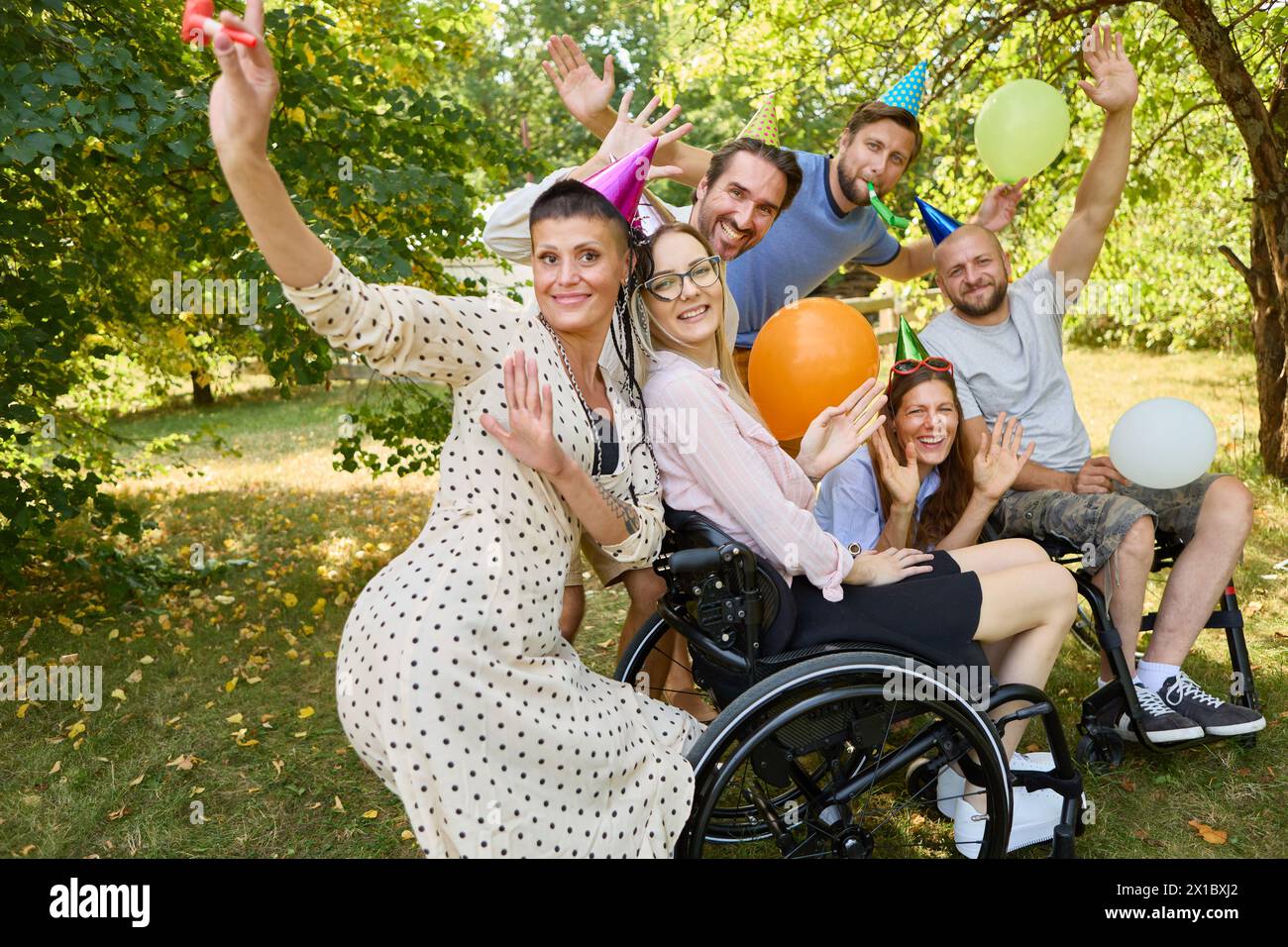 A joyous outdoor birthday celebration featuring a group of diverse friends, including a woman using a wheelchair, all enjoying with balloons and party Stock Photo
