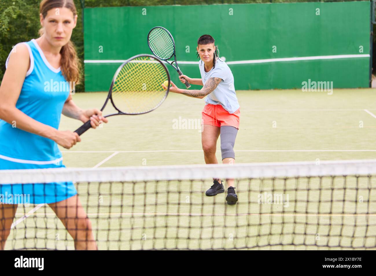 An inclusive sports scene with a woman using a lower limb prosthetic playing tennis against another woman on a green court. Showcasing mobility and co Stock Photo