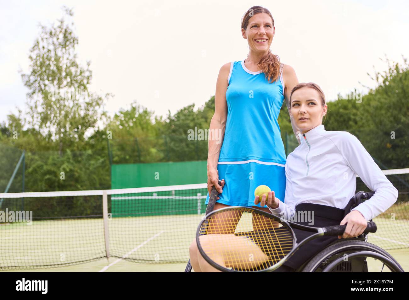 Two people spending time on a tennis court; one standing and one in a wheelchair, showcasing inclusion and active lifestyle. Stock Photo