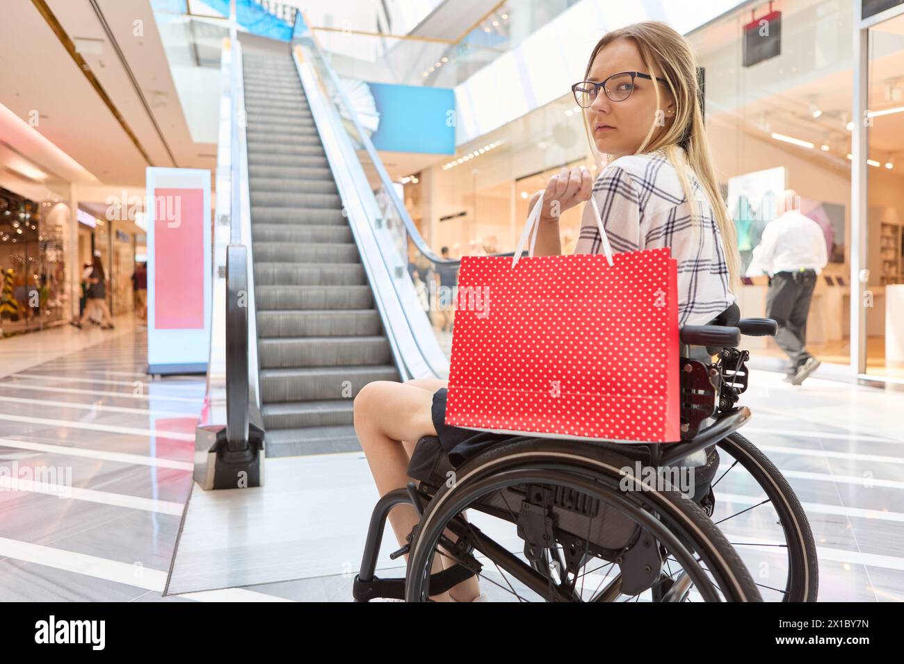 A person who uses a wheelchair holding a shopping bag while navigating the mall illustrates accessibility and independence. Stock Photo