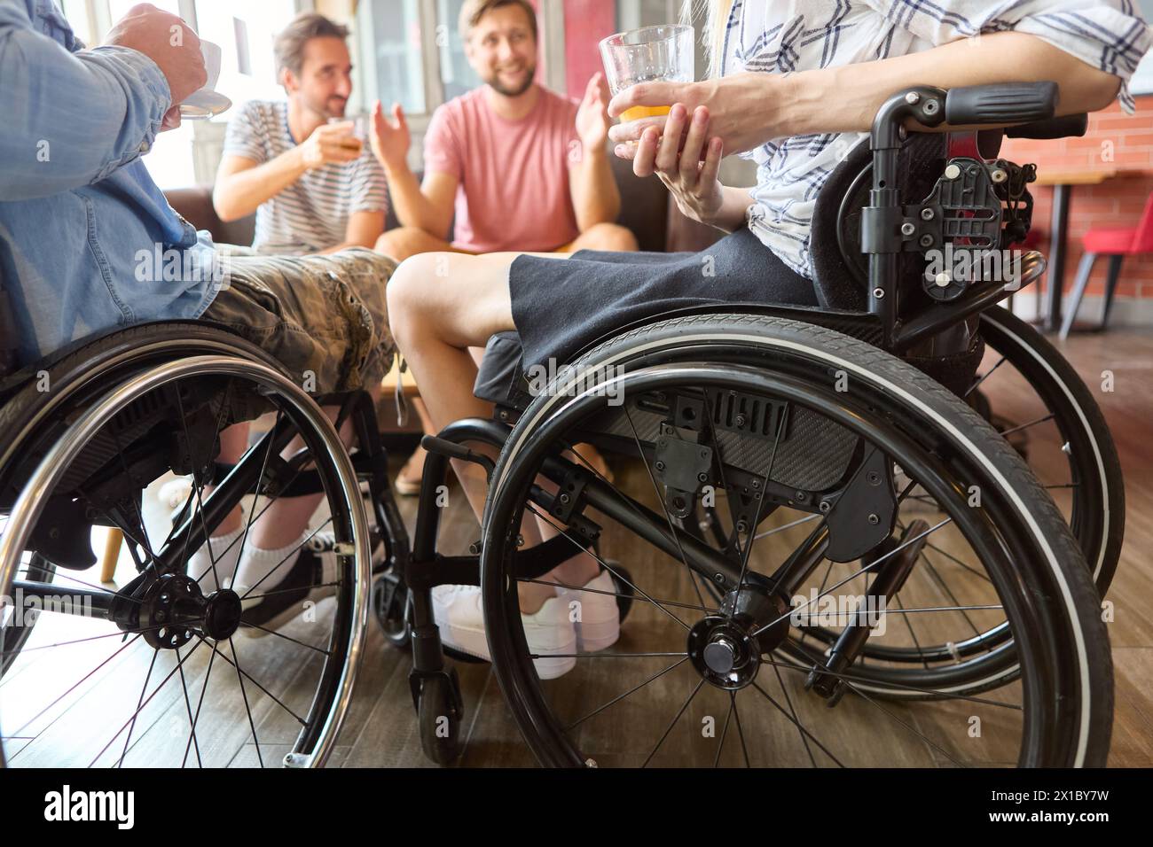 A friendly and inclusive social gathering at a cafe, featuring a person using a wheelchair engaged in a lively conversation with friends. Stock Photo