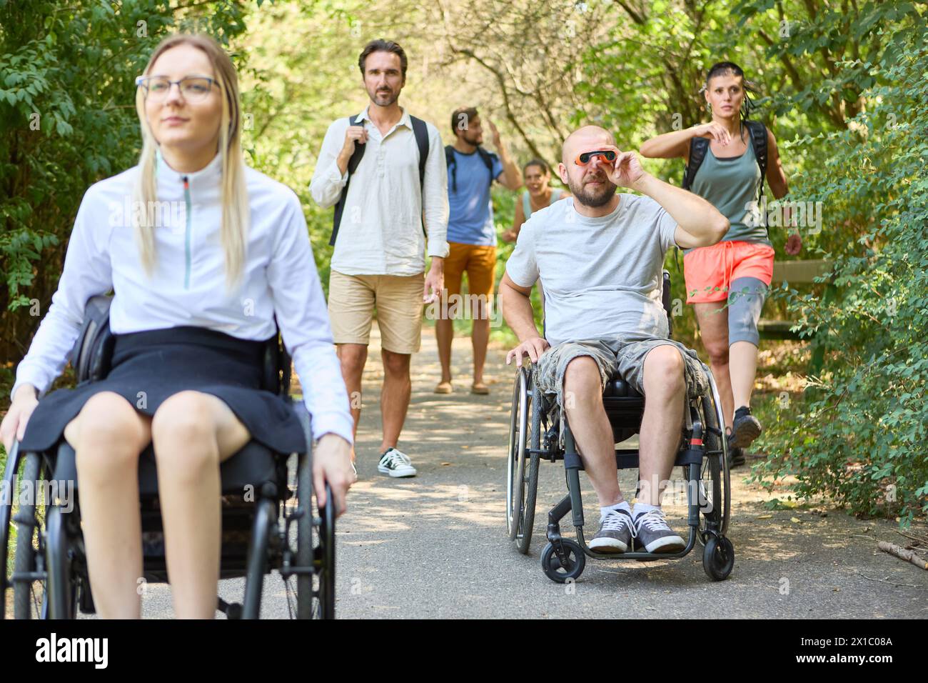 A group of friends, including individuals using wheelchairs, share a leisurely day outdoors, highlighting inclusion and accessibility. Stock Photo