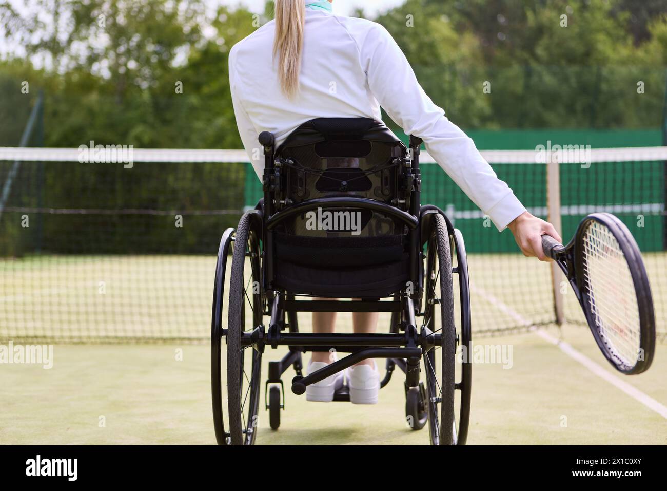 Focused and motivated, a person who uses a wheelchair holds a tennis racket on a court, showcasing accessibility and inclusion in sports. Stock Photo
