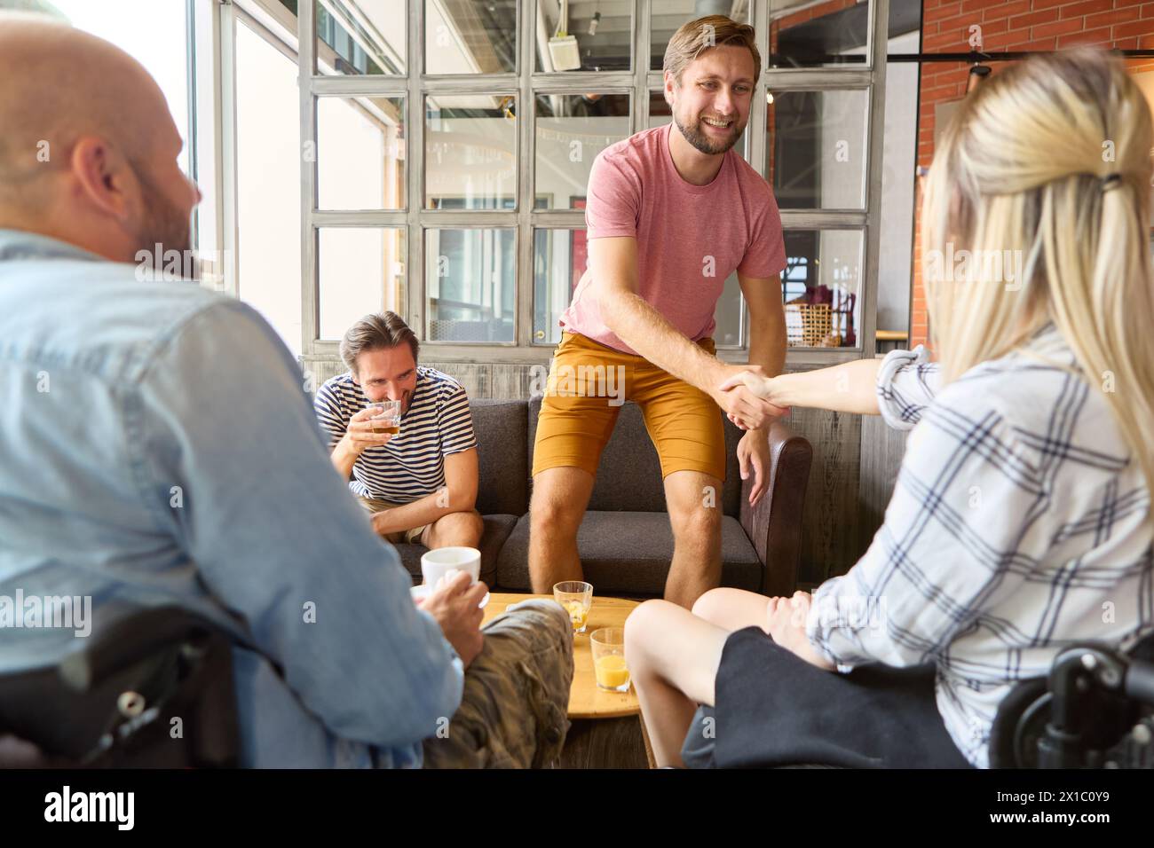 A friendly meeting in a cozy cafe with a diverse group of friends, including a person using a wheelchair. They are engaged in conversation, sharing la Stock Photo