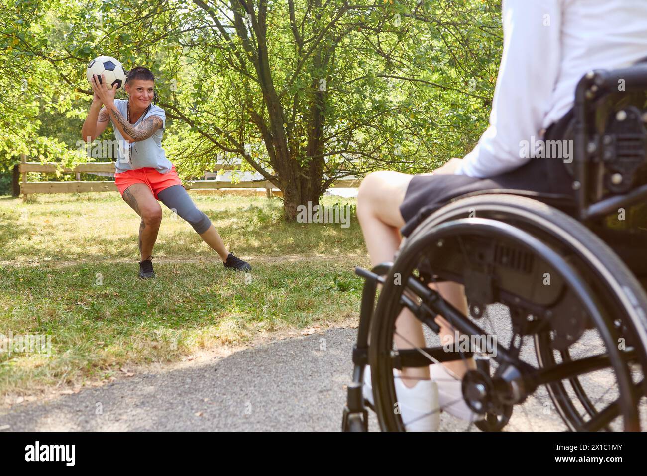 A person with a disability in a wheelchair and an able-bodied person enjoying soccer together outdoors, depicting inclusion and accessibility in sport Stock Photo