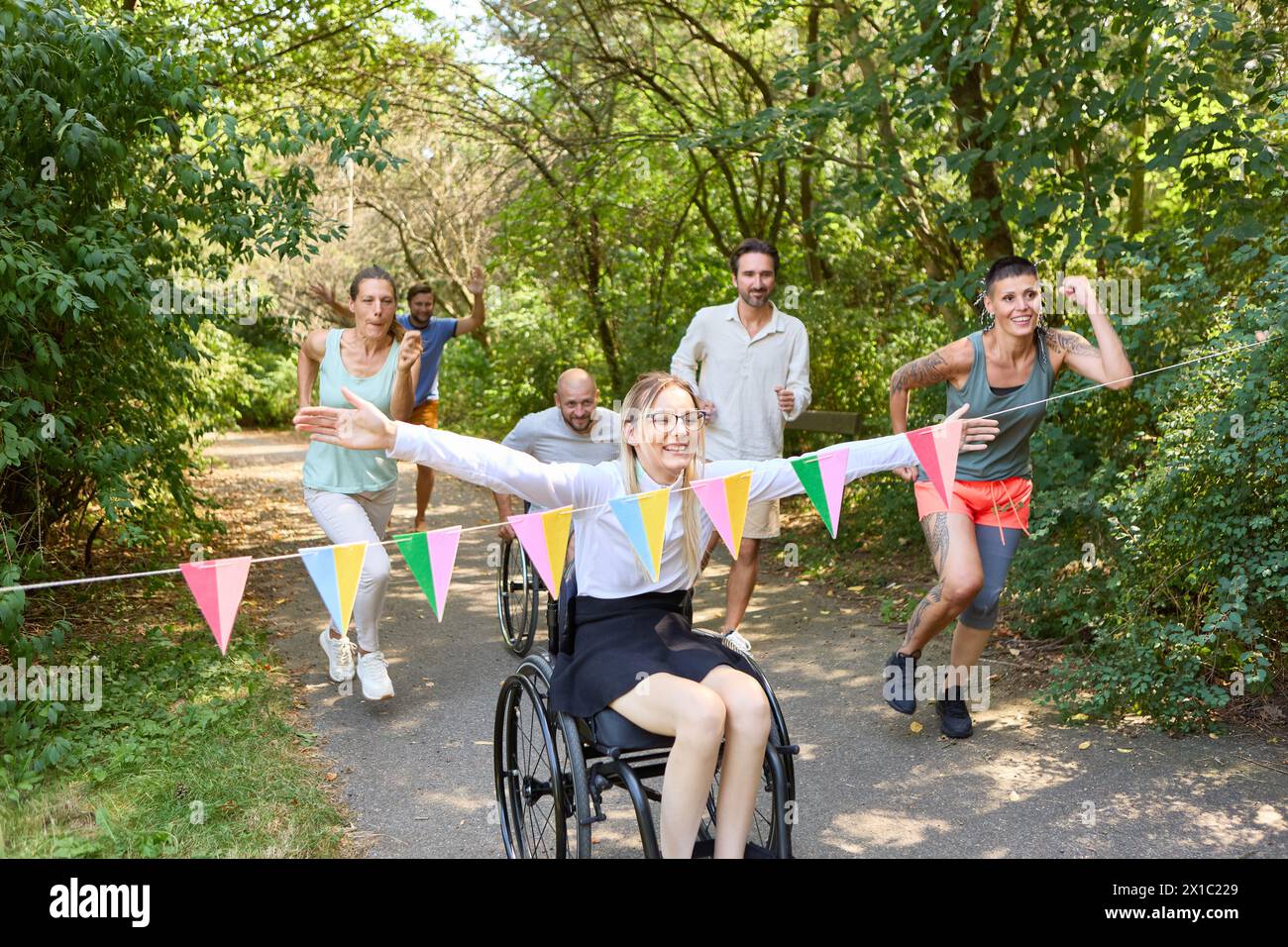 An inclusive outdoor event capturing a joyful race where a woman in a wheelchair competes with friends, embodying teamwork and diversity. Stock Photo