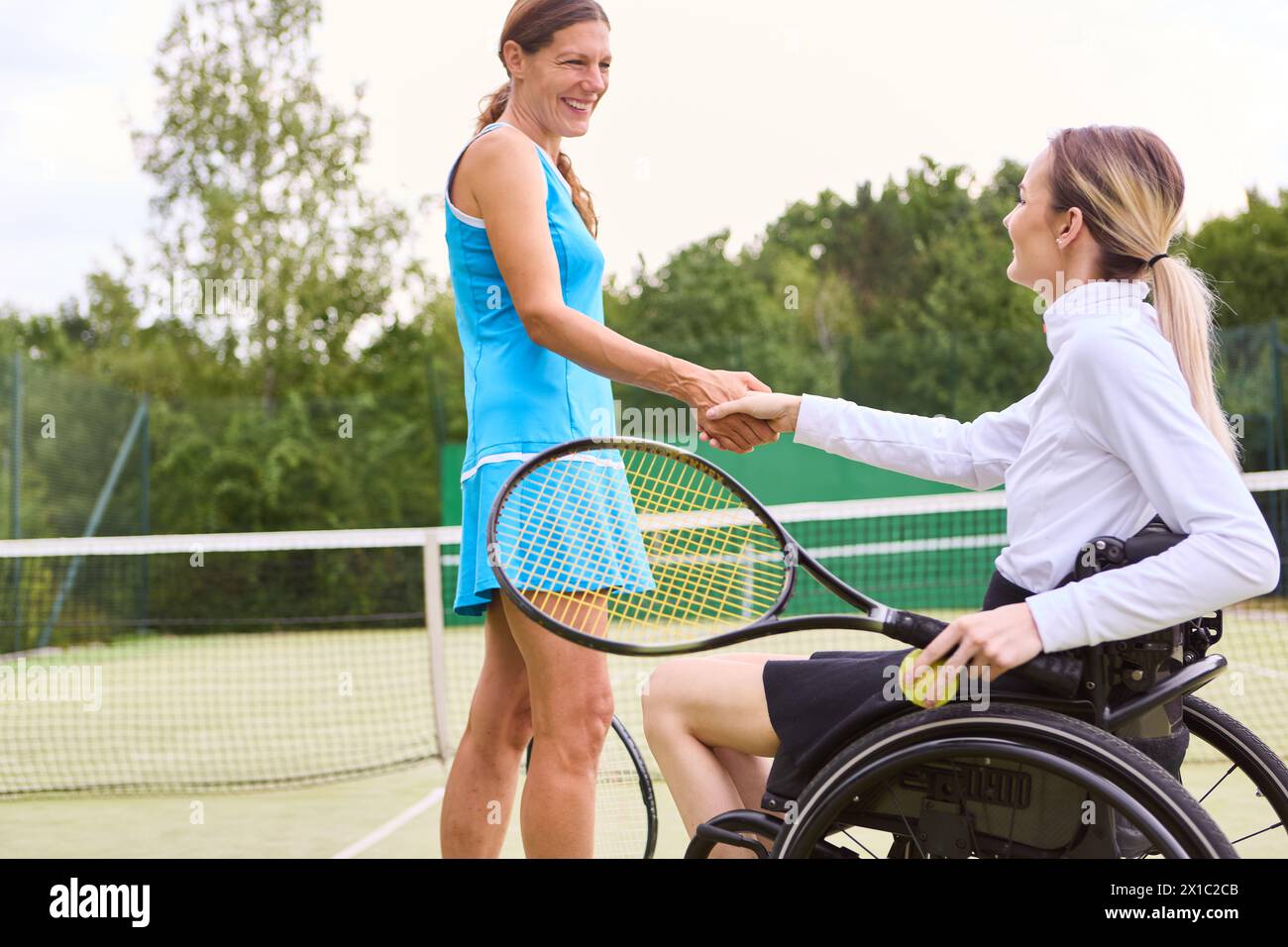 An athlete who uses a wheelchair celebrating teamwork with a standing player on a tennis court, promoting accessibility and inclusion. Stock Photo