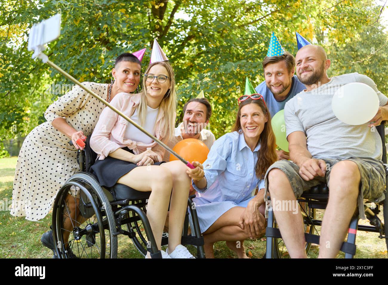 A joyful outdoor celebration featuring a group of friends, including people with disabilities, wearing party hats and enjoying a sunny day. Stock Photo
