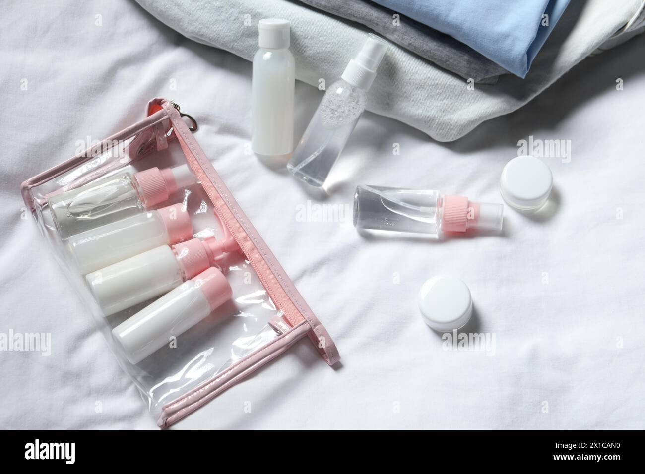 Cosmetic travel kit. Plastic bag with small containers of personal care products on bed Stock Photo