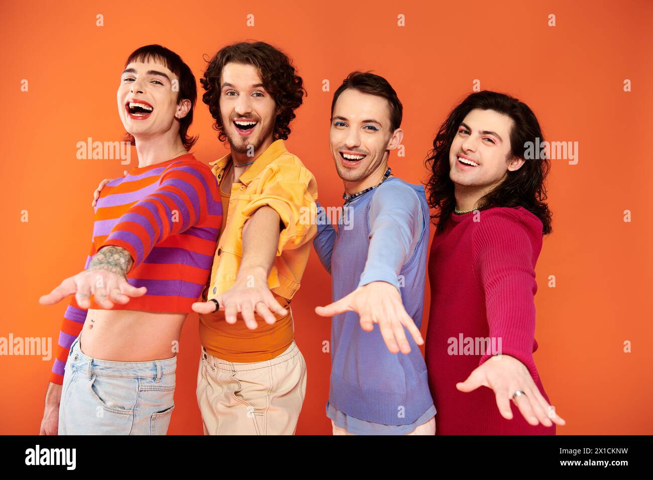 cheerful young gay men with makeup in vibrant attires posing actively together, pride month Stock Photo