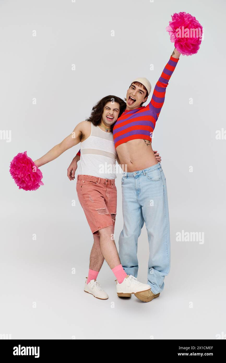cheerful young gay men in casual vivid attires posing happily with pom poms and looking at camera Stock Photo