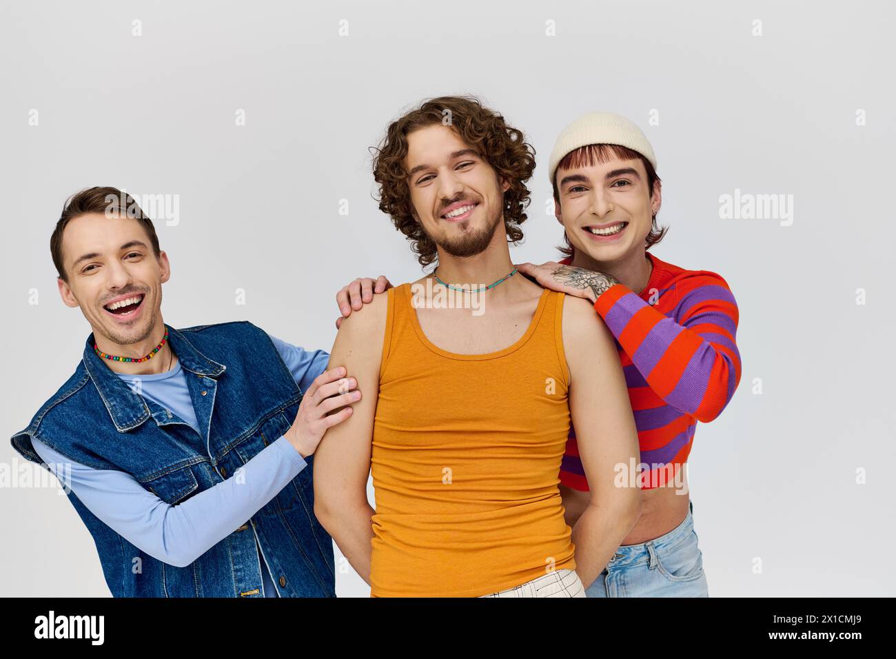 cheerful young gay men in vibrant attires posing together on gray backdrop and looking at camera Stock Photo