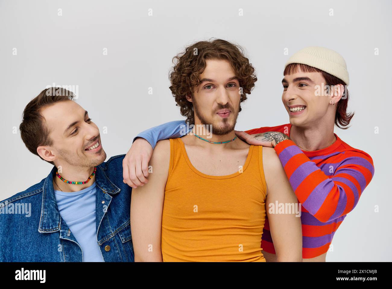 positive young gay men in vibrant attires posing together on gray backdrop and looking at camera Stock Photo