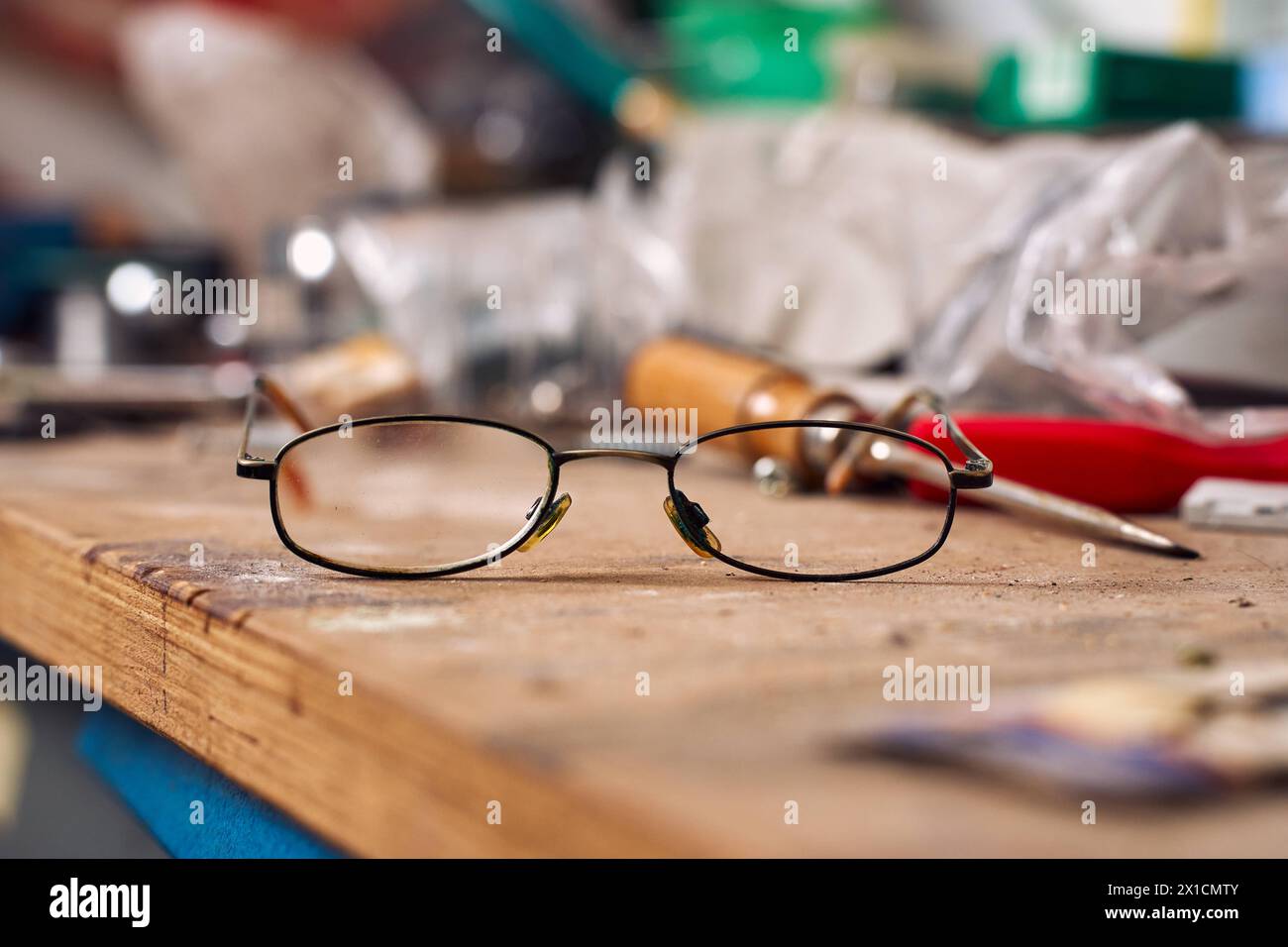 Augsburg, Bavaria, Germany - April 13, 2024: Broken old glasses on a workbench in a workshop. Symbolic photo work accident and insolvency *** Kaputte alte Brille auf einer Werkbank in einer Werkstatt. Symbolfoto Arbeitsunfall und Insolvenz Stock Photo