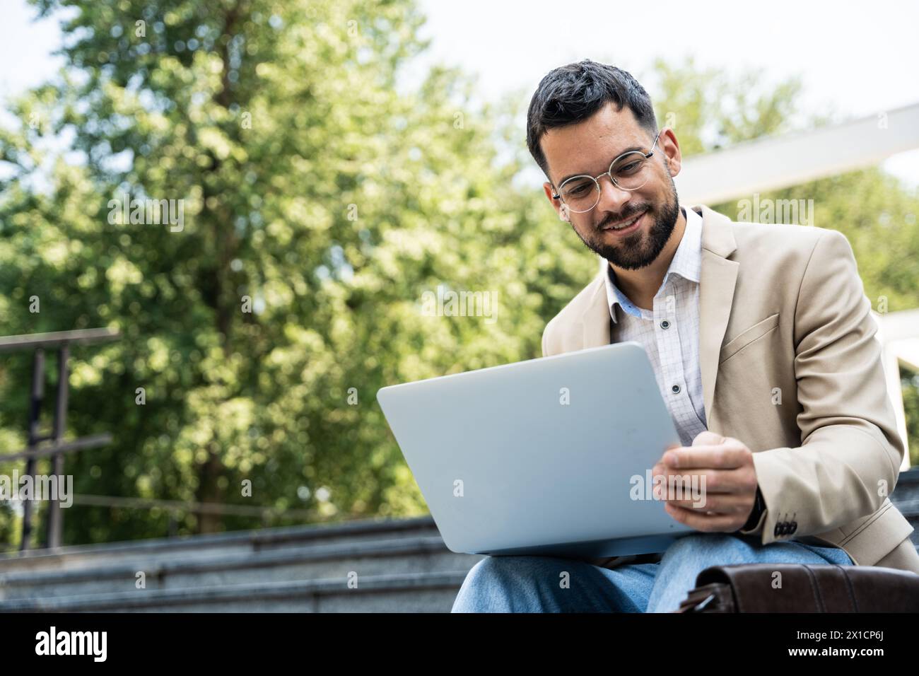 Young businessman in formal wear sitting on the stairs out of office building working on laptop computer. Job candidate work on application form befor Stock Photo