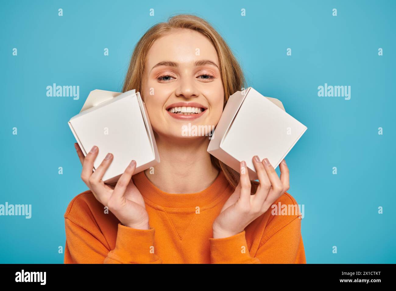 A beautiful blonde woman holds two food boxes in front of her face ...