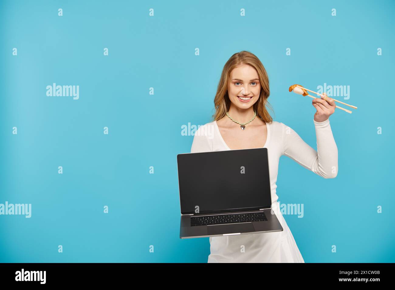 A blonde woman holding a laptop and Asian food, showcasing a blend of technology and culinary delights. Stock Photo
