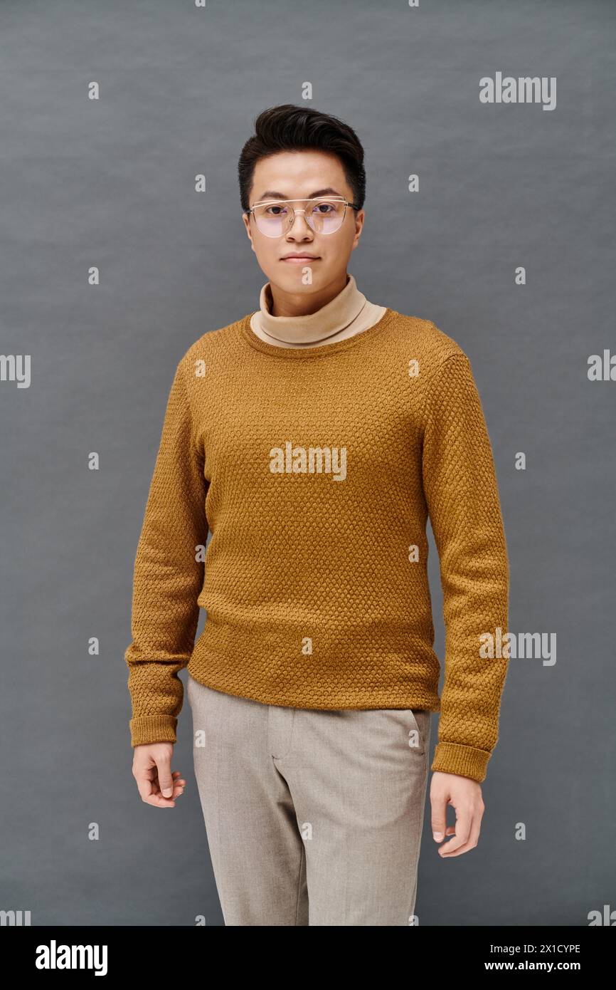 A fashionable young man in a brown sweater and tan pants poses confidently, showcasing his elegant attire. Stock Photo