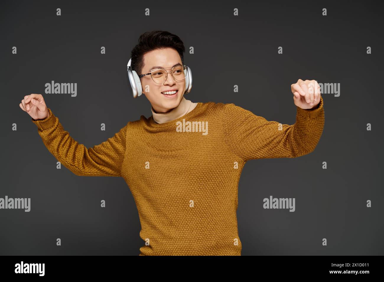 A fashionable young man energetically poses in a cozy sweater while wearing headphones, exuding a trendy and sophisticated vibe. Stock Photo