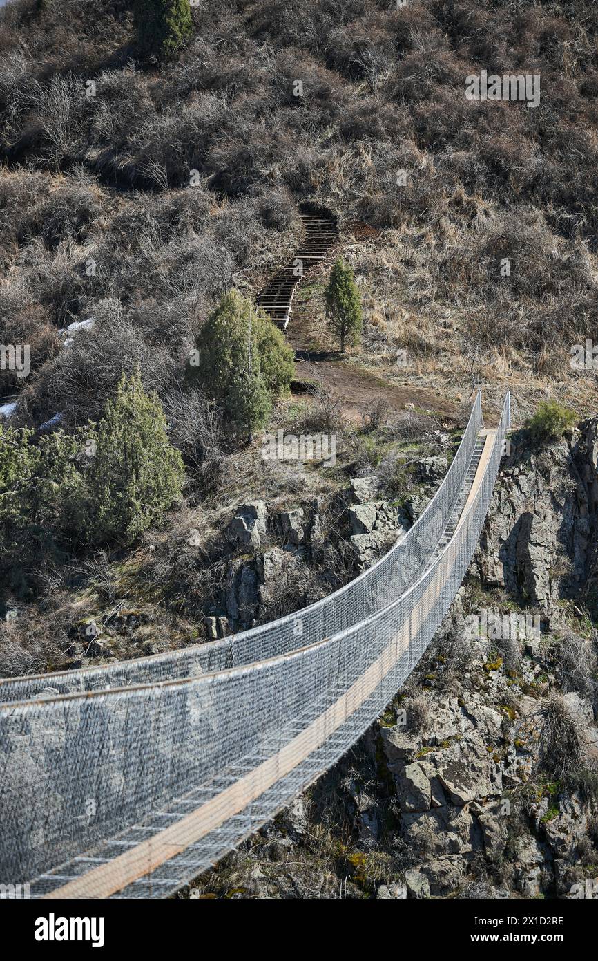 Suspension excursion bridge over gorge. Sightseeing holiday tour, Kyrgyzstan. Crossing between two mountains. Dangerous footbridge, frightening path f Stock Photo