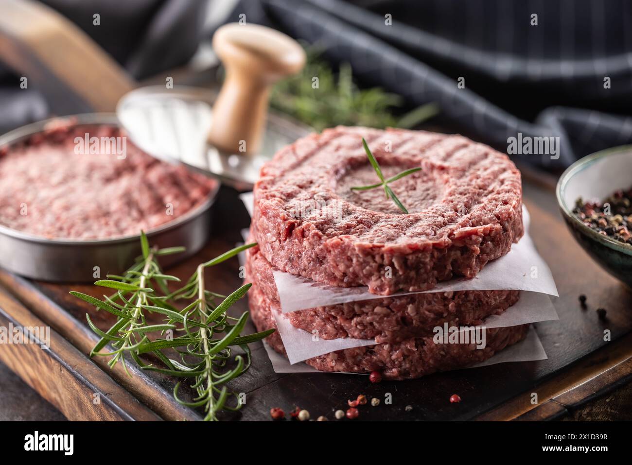 Fresh raw ground beef patties with rosemary salt and pepper made in a meat form on a cutting board. Stock Photo