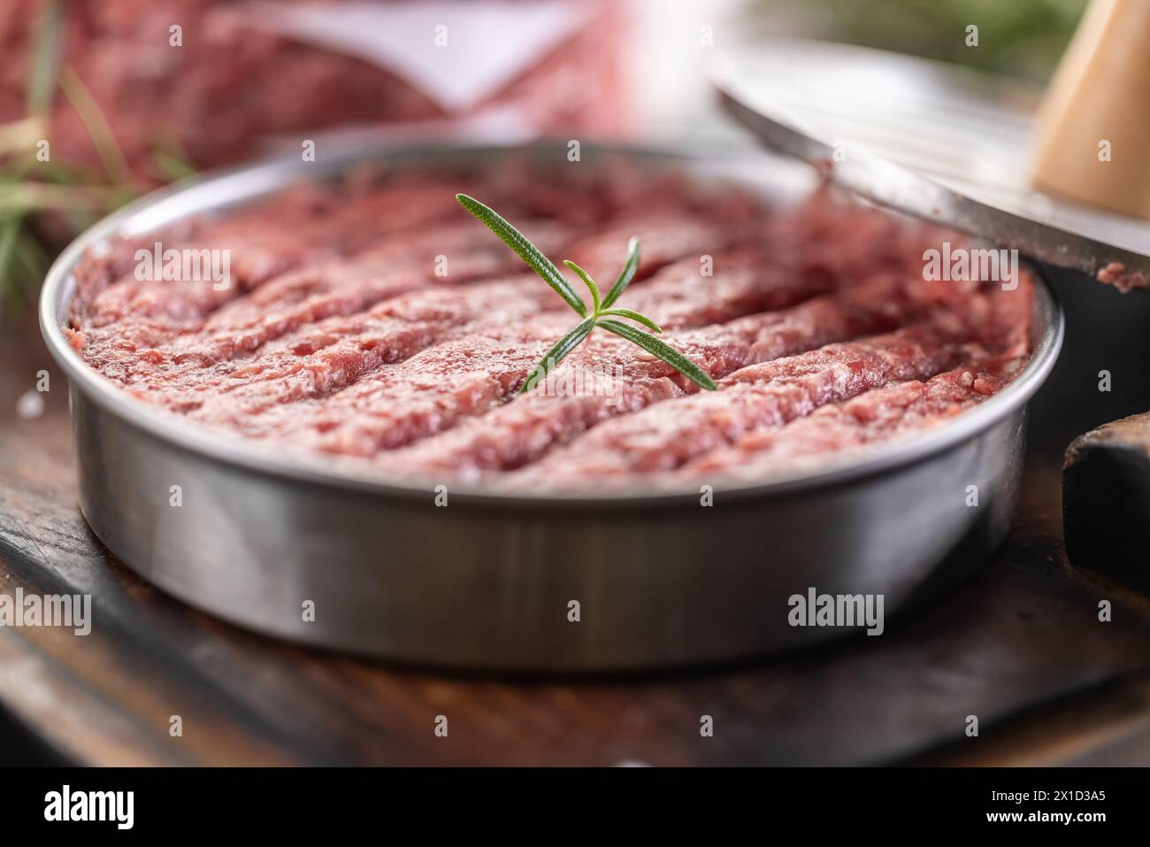 Fresh raw ground beef patties with rosemary salt and pepper made in a meat form on a cutting board. Stock Photo
