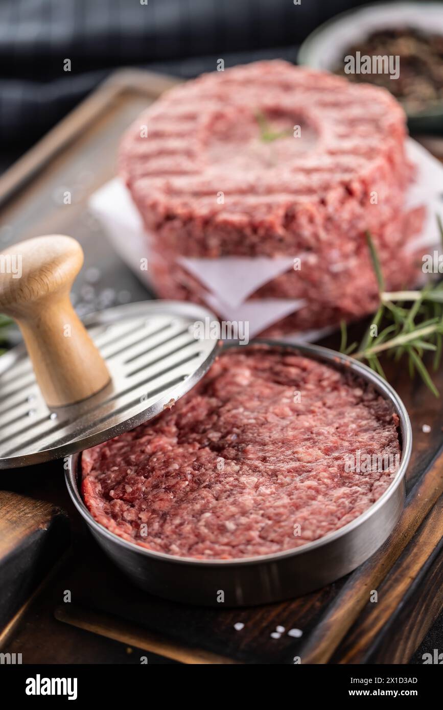 Fresh raw ground beef patties with rosemary salt and pepper made in a meat form on a cutting board. Stock Photo