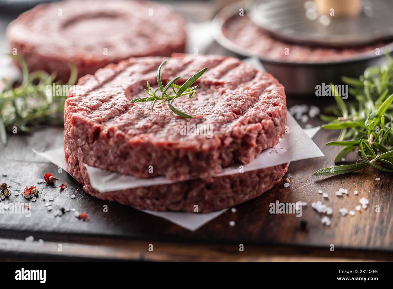 Fresh raw ground beef patties with rosemary salt and pepper made in a meat form on a cutting board. Stock Photo