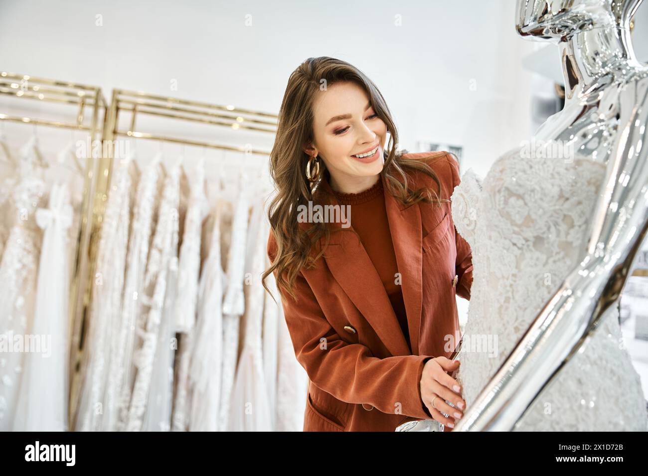 A young bride-to-be stands next to a mannequin wearing a bridal gown, deciding on her wedding dress. Stock Photo