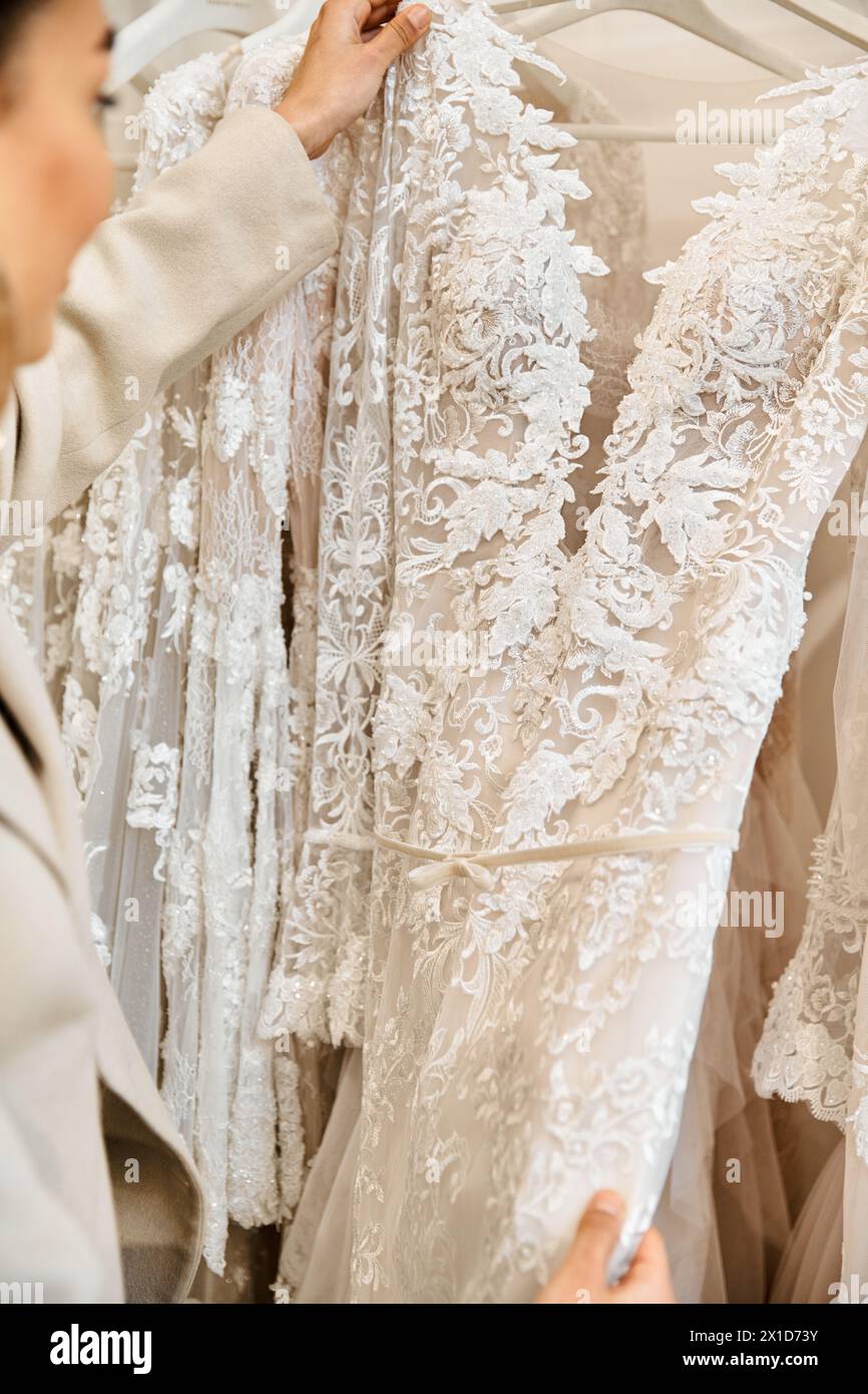 A young bride, carefully examines a dress on a rack in a bridal boutique. Stock Photo