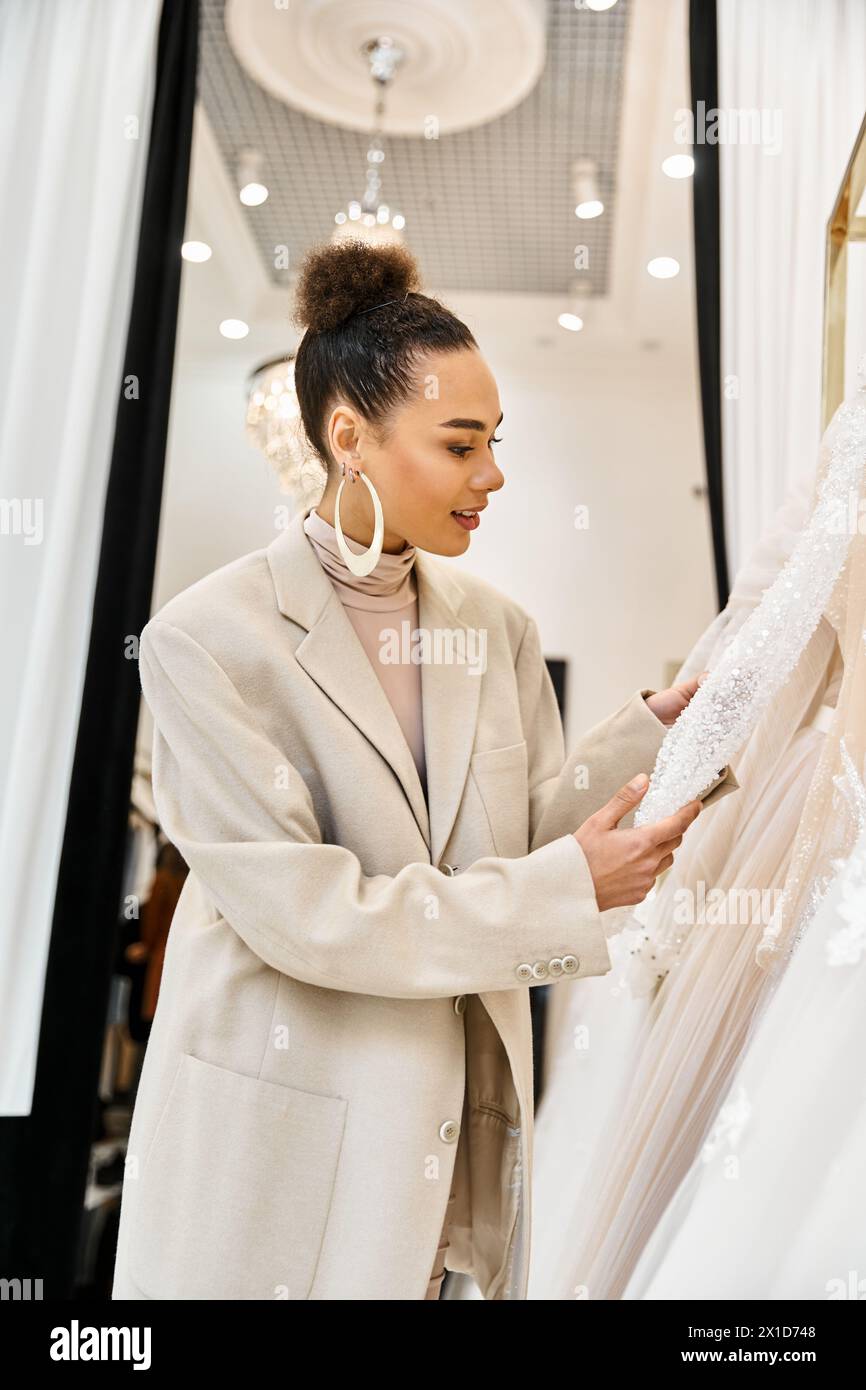 A young beautiful bride standing next to a white wedding dress, in a bridal boutique. Stock Photo